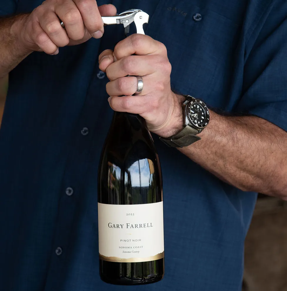 Man opening a bottle of Gary Farrell wine with a corkscrew